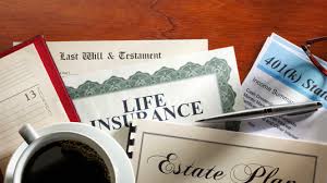 An assortment of financial and legal documents, including a Last Will and Testament, Life Insurance policy, 401(k) Statement, and Estate Plan binder, arranged on a wooden desk with a coffee mug and pen.