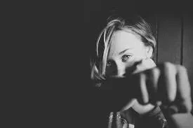 A black and white close-up shot of a woman looking intently forward while holding her clenched fist directly toward the camera.